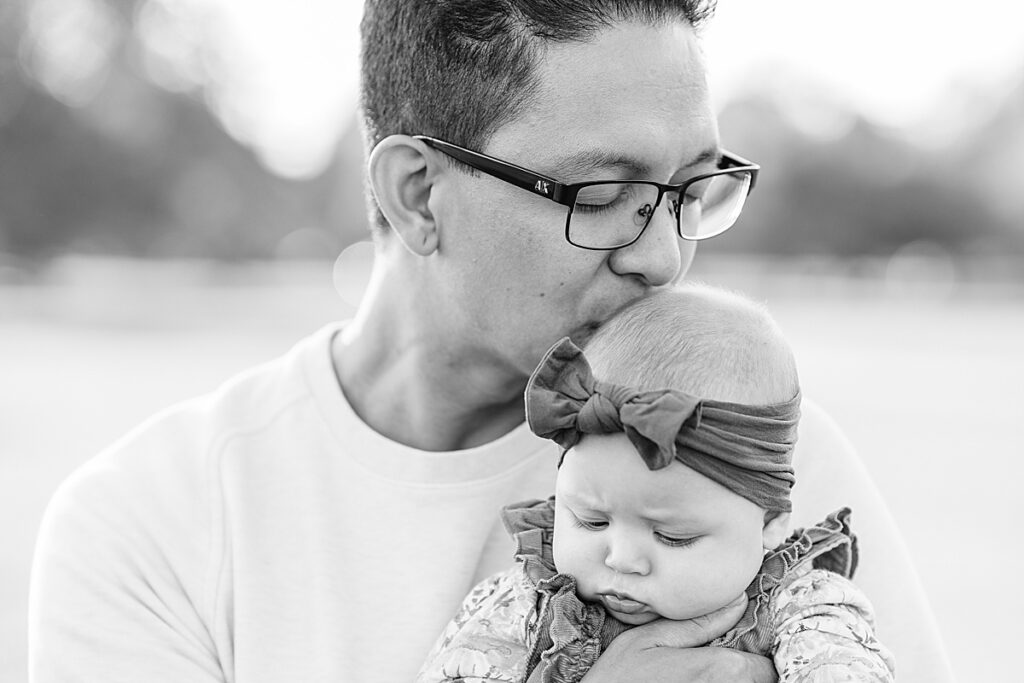 Black and white photo of man with black glasses kissing baby on head