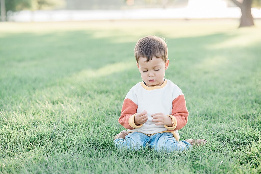 Boy in blue jeans and orange and white sweater kneeling in grass