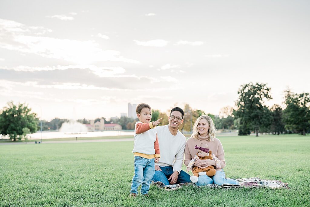 Young boy standing in front of man and woman with baby pointing at the camera