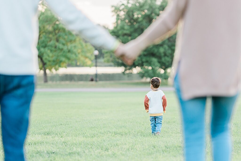 Man in white sweater and woman in white sweater holding hands with boy running in between