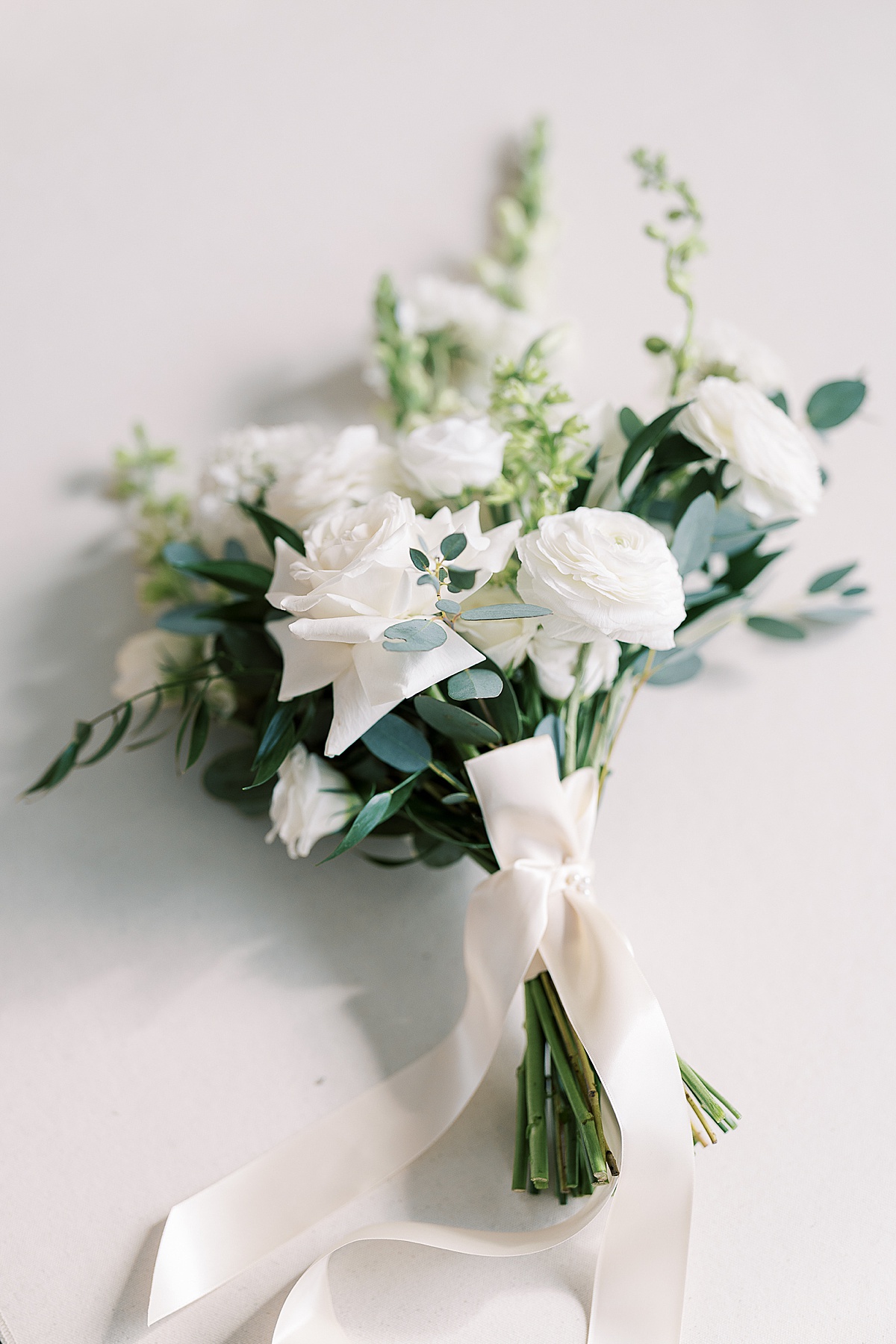 White wedding flowers with white ribbon laying on white background