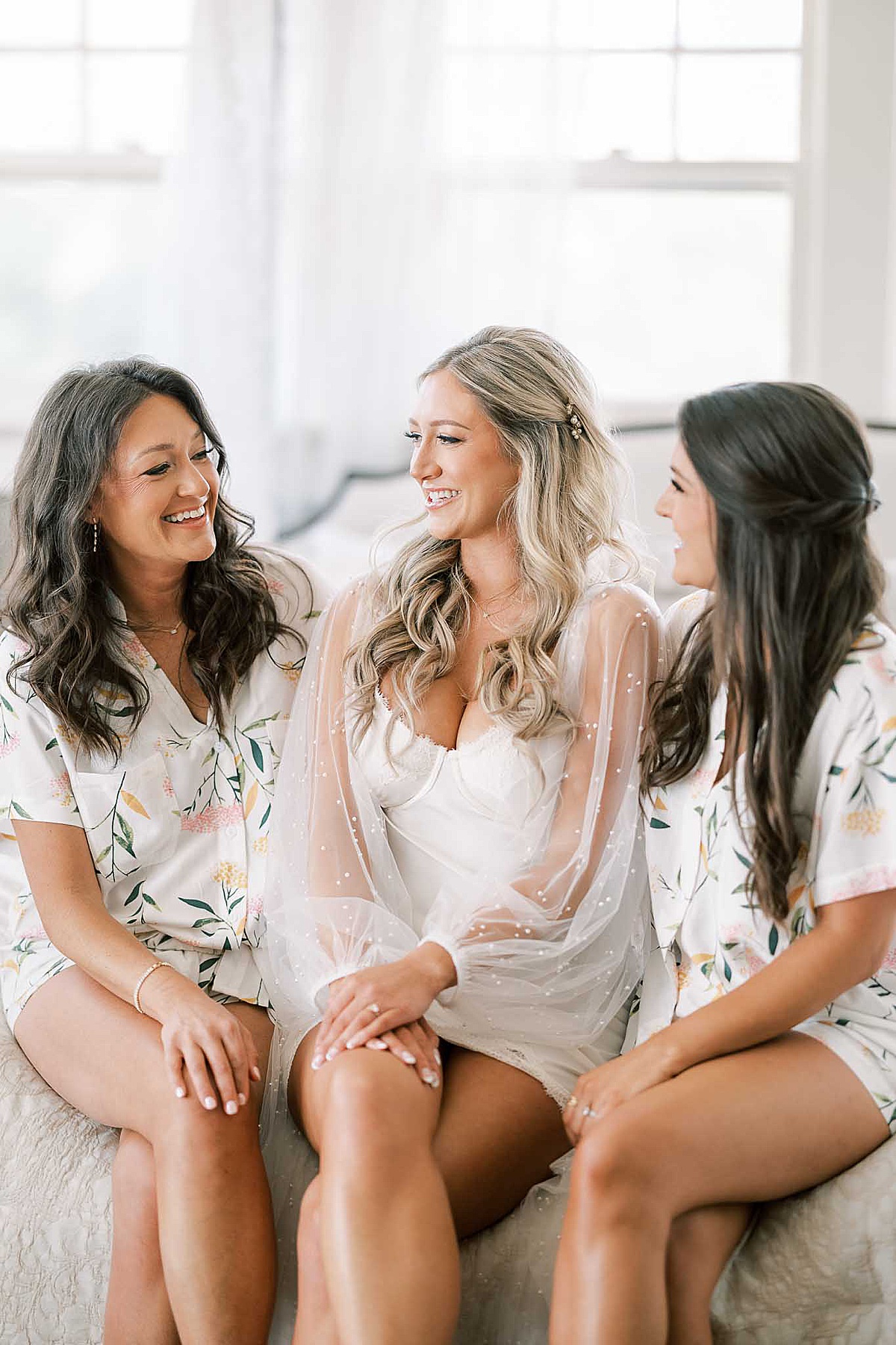 Bride sitting with two bridesmaids on bed