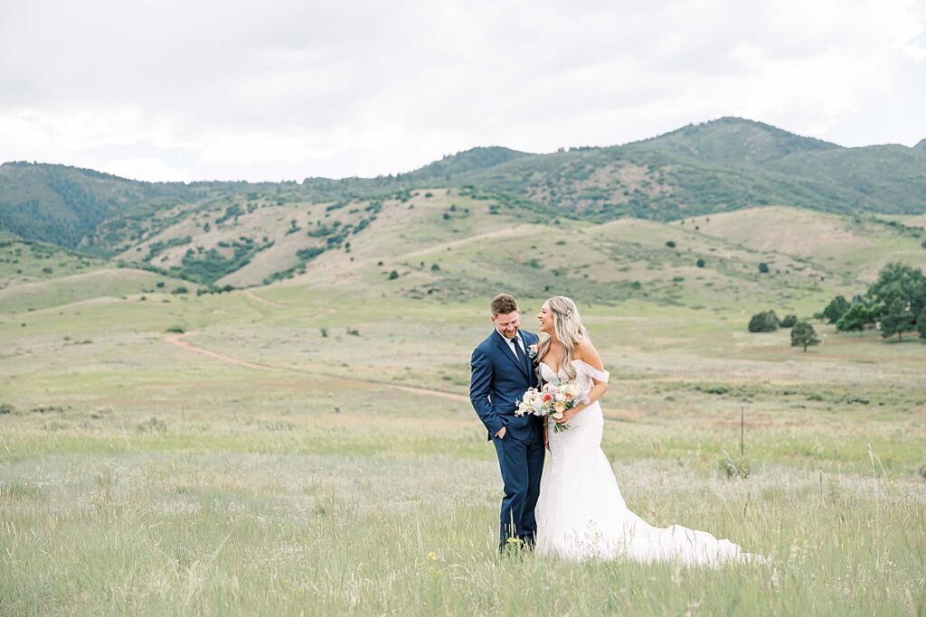 Bride and groom standing in field laughing