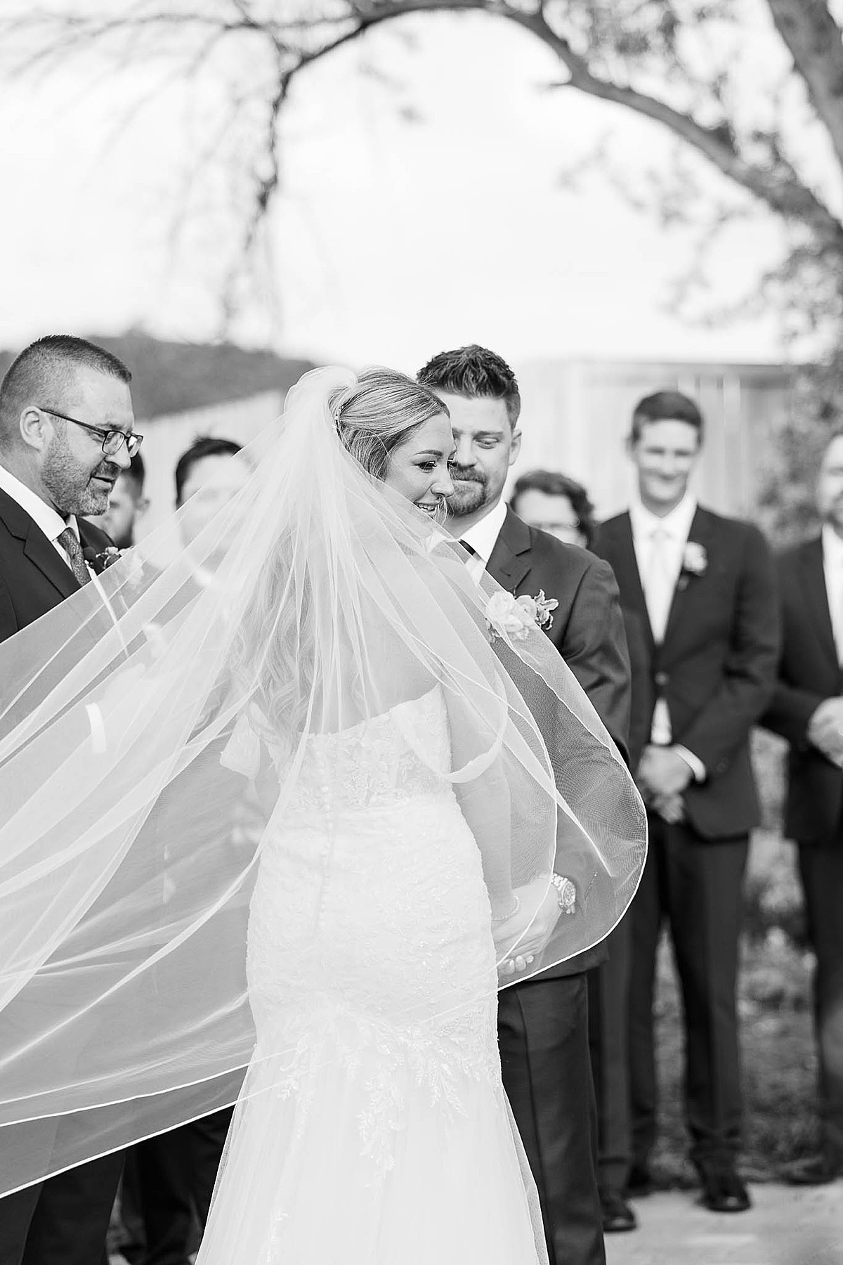 Black and white photo of bride's veil blowing away during ceremony