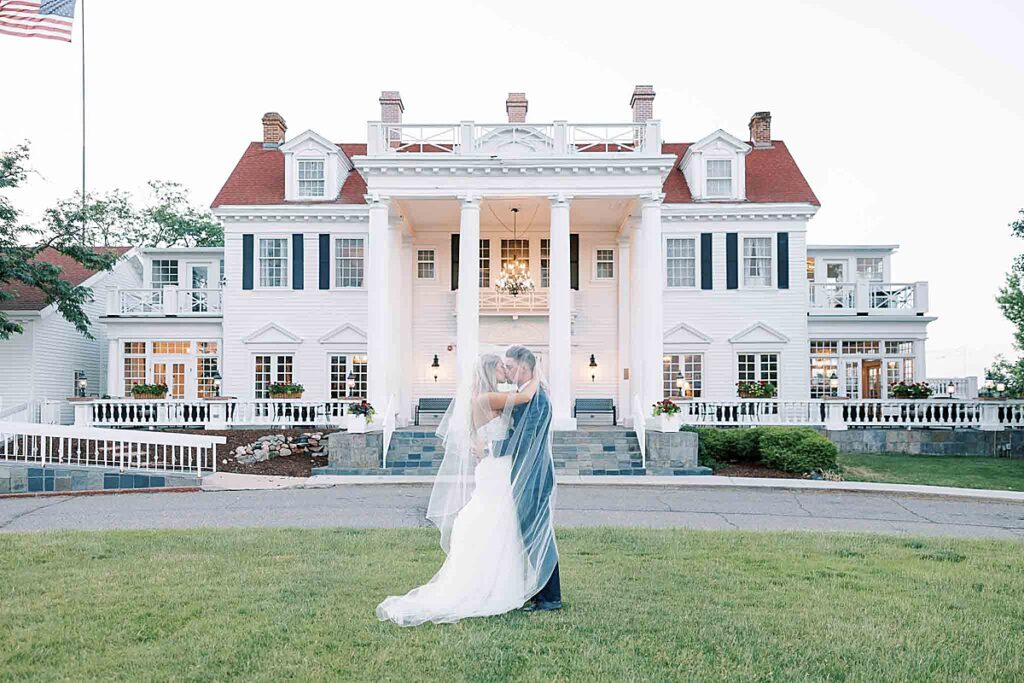 Couple kissing under veil in front of large white wedding venue