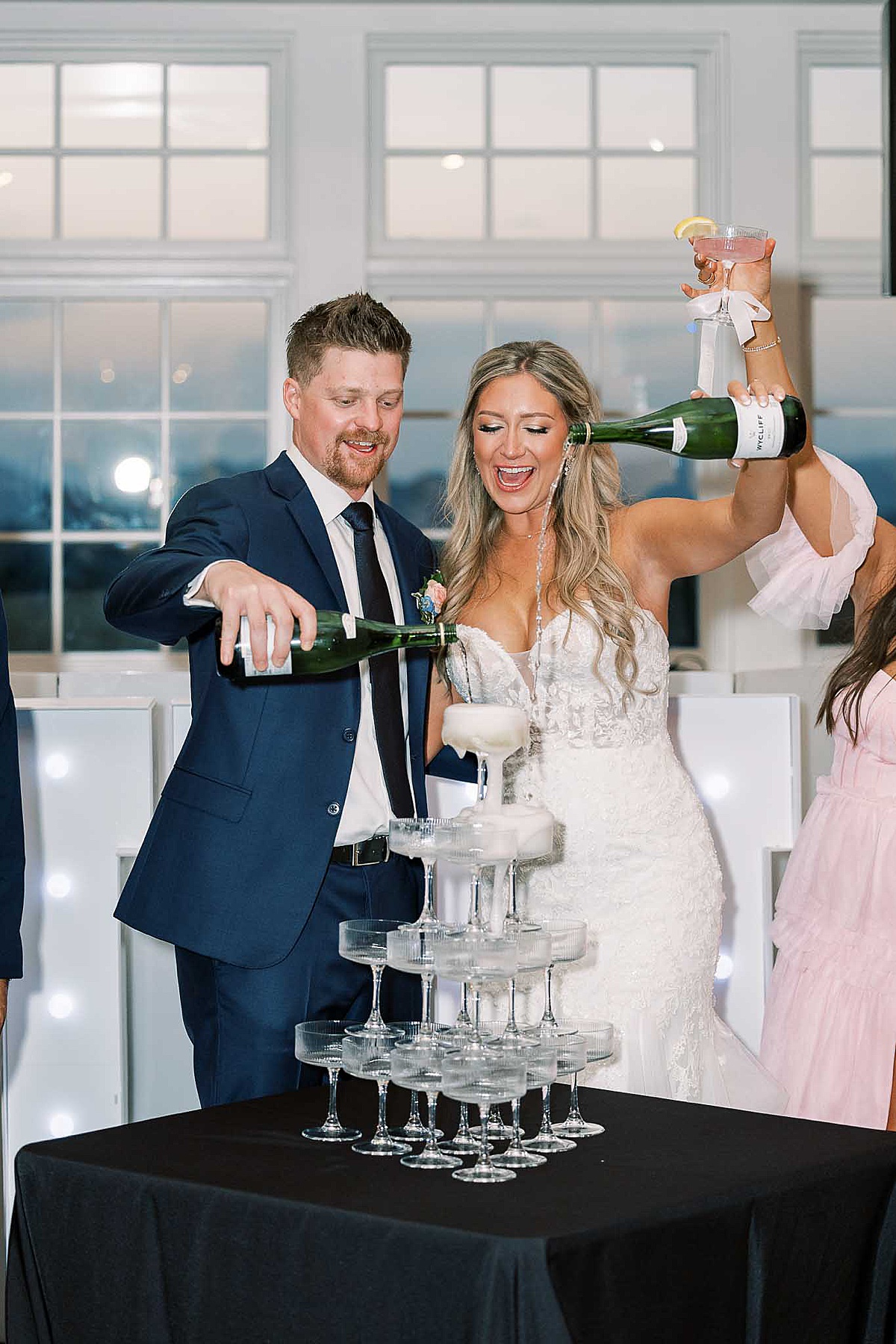 Bride and groom pouring champagne into a champagne tower on black tablecloth